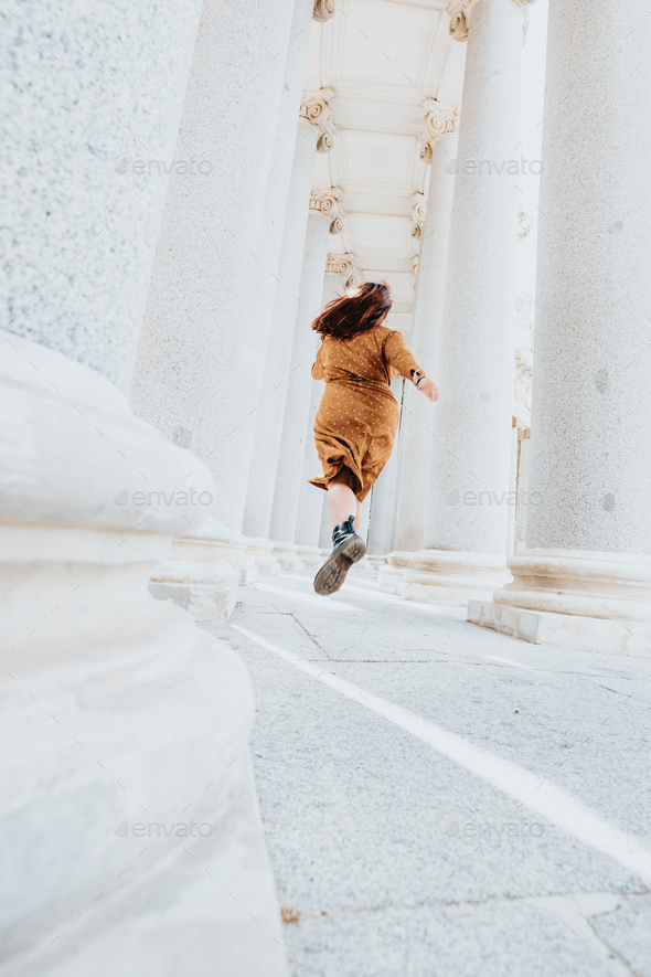 Stylish girl in orange dress running through a white corridor in hipster movie indie vibes