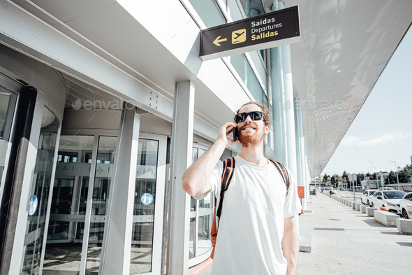 Handsome young hipster man with street clothes talking on phone near airport