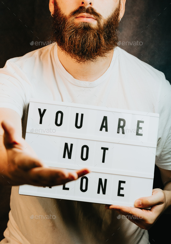 Young bearded hipster man holding a sign that says you are not alone