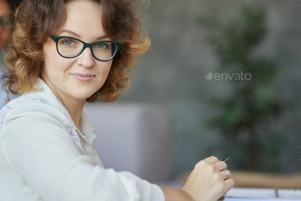 Kind teacher. Portrait of attractive young female teacher in glasses smiling at camera while having
