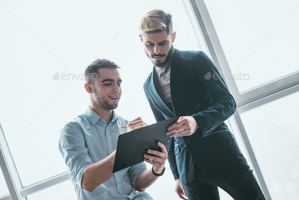 Two focused male co-workers deep in discussion together, making notes, smiling, while standing in a - Stock Photo - Images