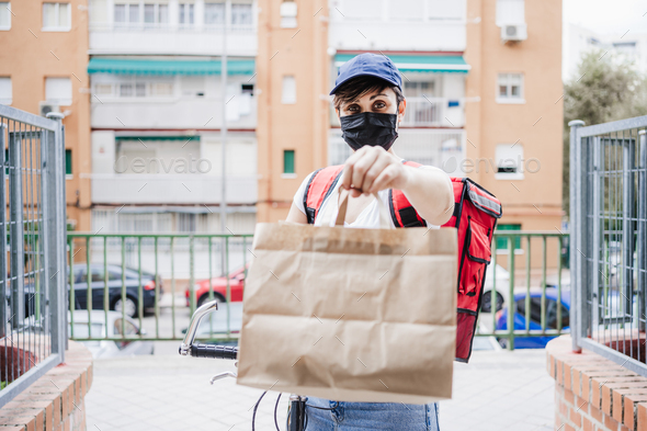 young woman rider delivering meal with bicycle while wearing mask for corona virus pandemic