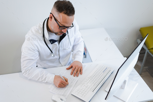 Male doctor filling medical documentation while sitting at his workplace in the office