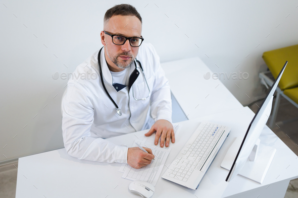 Male doctor filling medical documentation while sitting at his desk in the office