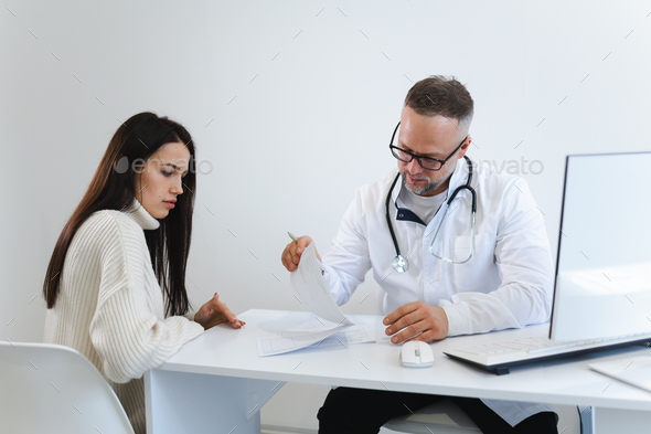 Male doctor fills out medical documentation during the female patient\'s appointment