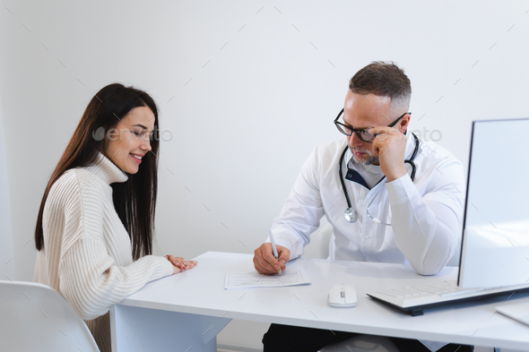 Male doctor writing a prescription for her patient. Woman at the physician office