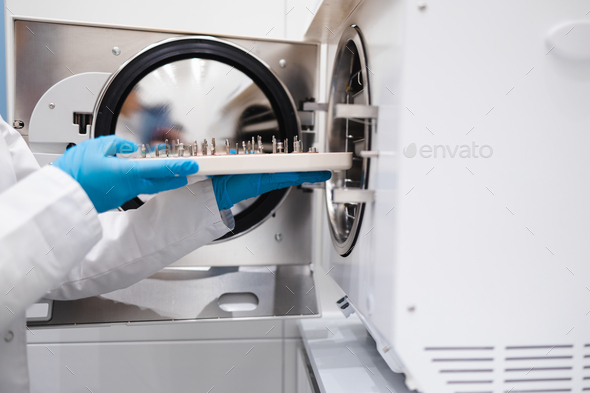 Close-up view of the hands of female dentistry worker who puts a dental instrument into autoclave.