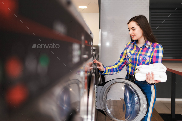 Girl in the public laundry. Laundromat client pays in the washing machine