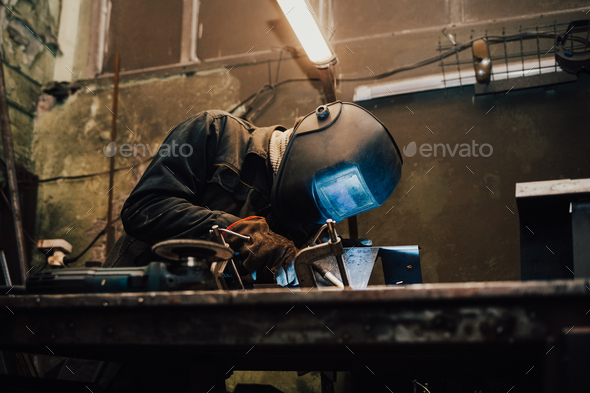 Worker in a welder mask works in a workshop for welding iron. Man makes iron products.