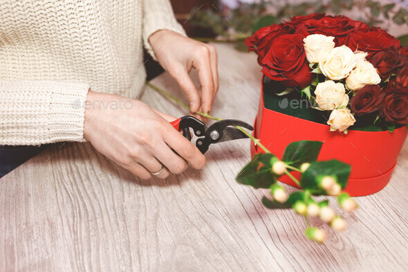 Flower shop seller prepares roses to create a bouquet by pruning them with pruners