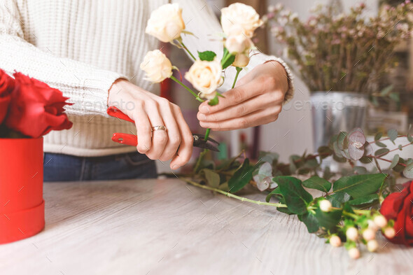 Flower shop seller prepares roses to create a bouquet by pruning them with pruners