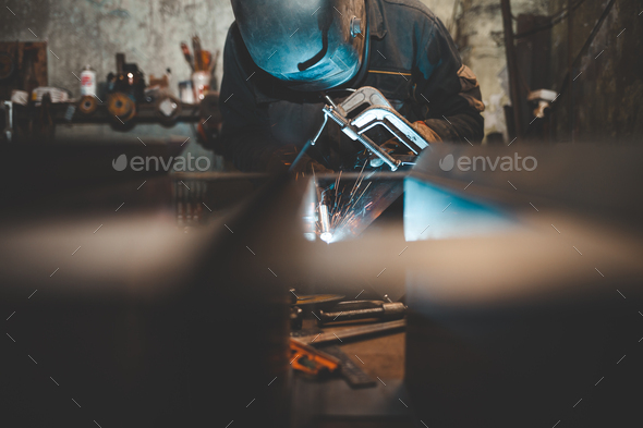Worker in a welder mask works in a workshop for welding iron. Man makes iron products.