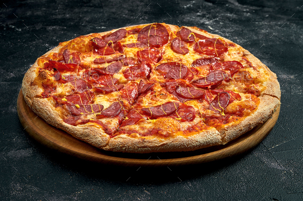 Pizza with salami and smoked sausages on a black stone background. 45 degree angle view