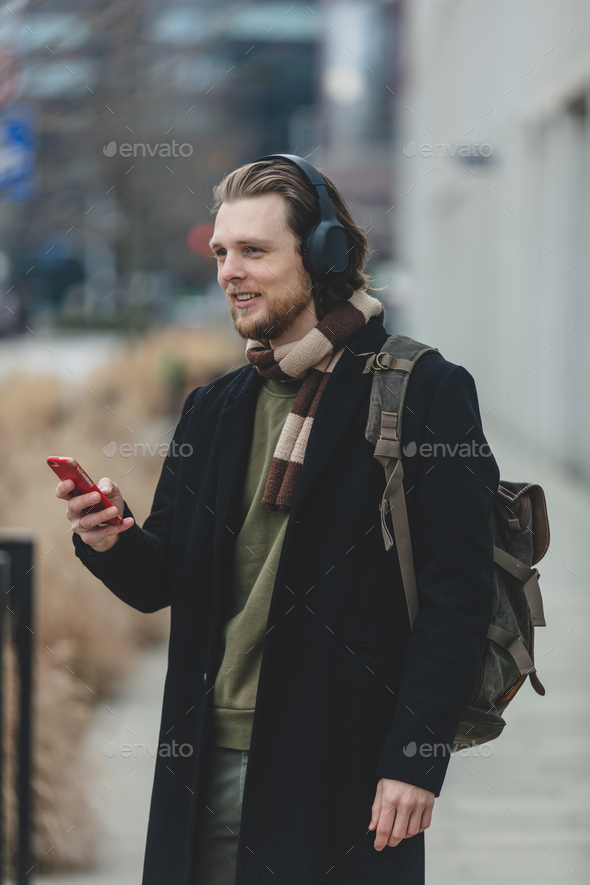 stylish guy in scarf and coat listen a music on streaming service by using mobile phone