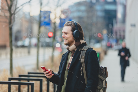 stylish guy in scarf and coat listen a music on streaming service by using mobile phone