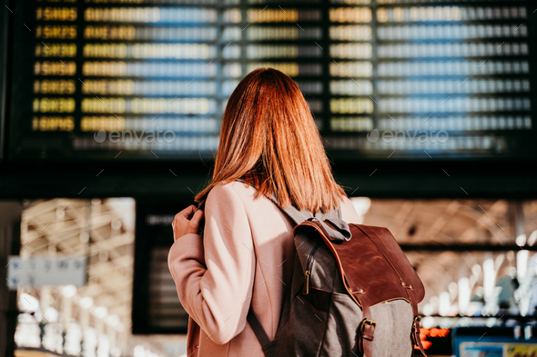 young woman at train station looking at destination board. Travel and public transport concept