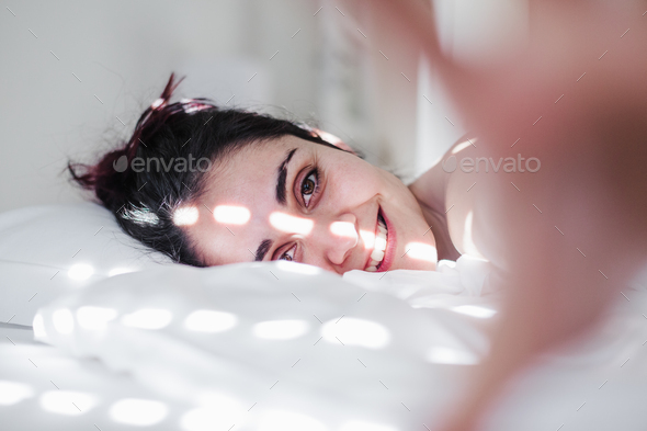 portrait of attractive young caucasian woman relaxing in bed during morning time.