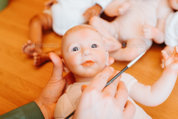 Reborning, handmade craft doll. Close-up puppet master holding realistic doll of newborn caucasian