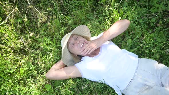 Happy Smiling Elderly Senior Woman in Straw Hat Lying on Grass Suffering From Mosquito Insects in