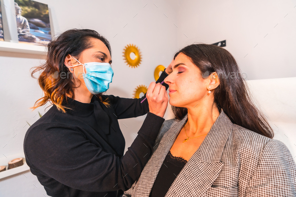 Makeup artist with face mask applying makeup to the client\'s eyes