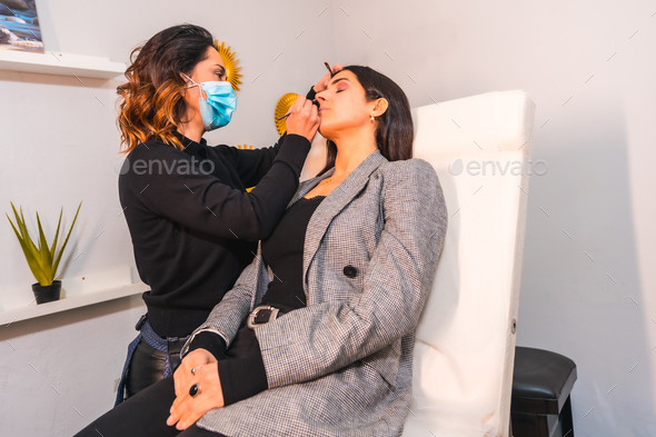 Makeup artist with face mask applying makeup to the client's eyes
