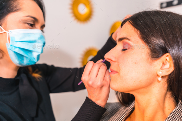 Makeup artist with face mask applying makeup to the client\'s eyes