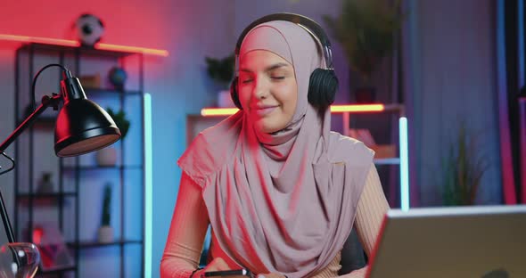 Lady in Hijab in Headphones Listening Music in Beautifully Decorated Room with Colourful lighting alt