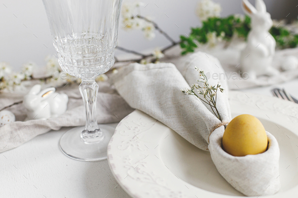Easter egg in bunny napkin, plate, cutlery, flowers. Stylish elegant Easter brunch table setting