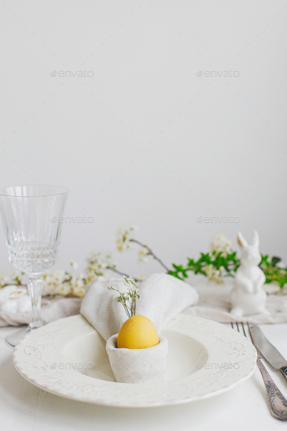 Easter egg in bunny napkin on plate, cutlery, flowers. Stylish elegant Easter brunch table setting