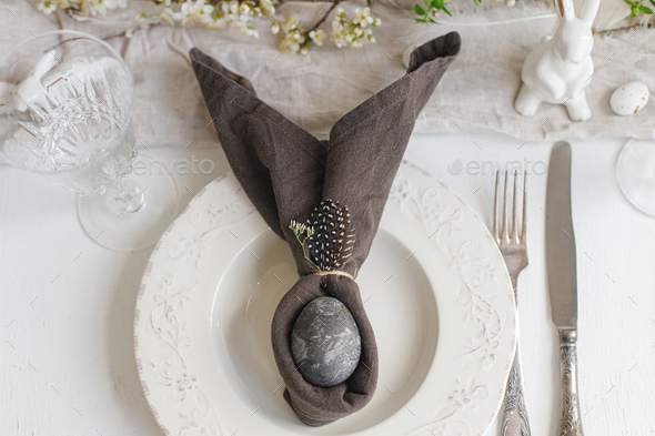 Happy Easter! Stylish elegant Easter brunch table setting. Easter egg in bunny napkin on plate
