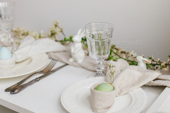 Stylish elegant Easter brunch table setting. Easter egg in bunny napkin, plate,cutlery, flowers