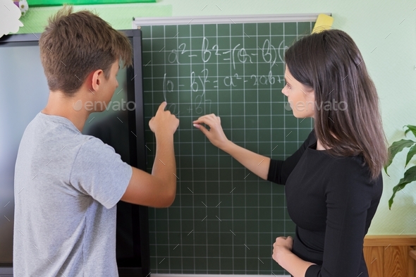 Male teenager student with teacher near school chalk board at math lesson