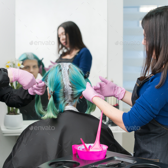 Process of hair dye in beauty salon. Two hairdressers apply paint hair during bleaching hair roots