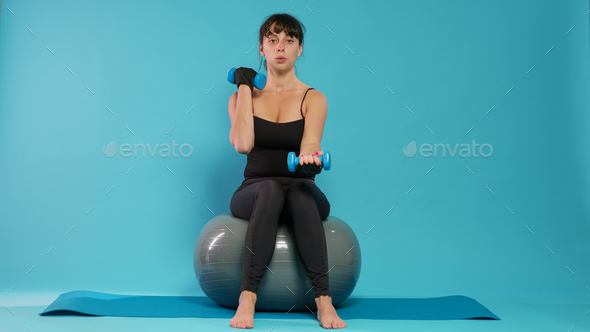 Fit person using dumbbells to lift weights on fitness toning ball