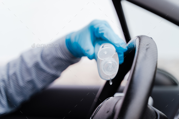 unrecognizable man in a car using alcohol gel to disinfect steering wheel during pandemic