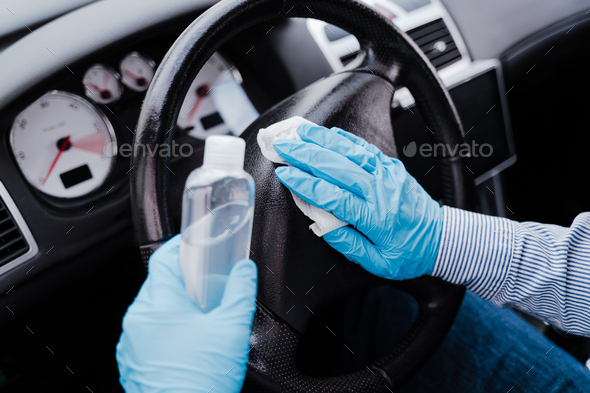 unrecognizable man in car using alcohol gel to disinfect steering wheel during pandemic