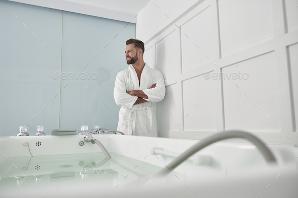 Attractive man with crossed arms stands near hydro massage tub in spa salon