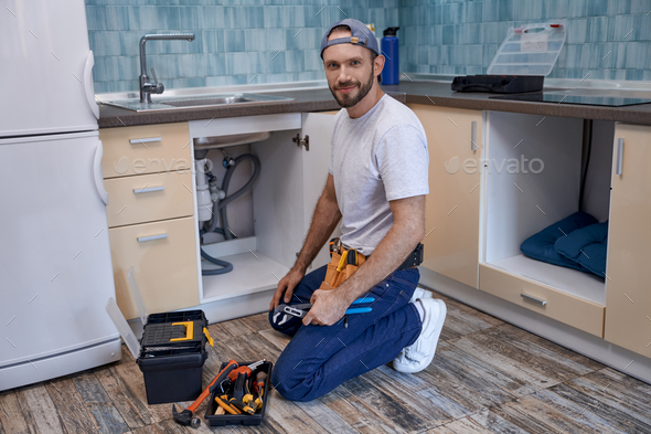 Young caucasian male worker on floor next to kitchen sink