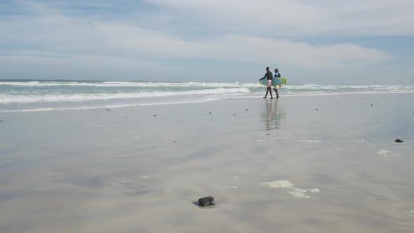 African american father and teenage son walking on a beach holding surfboards and talking alt