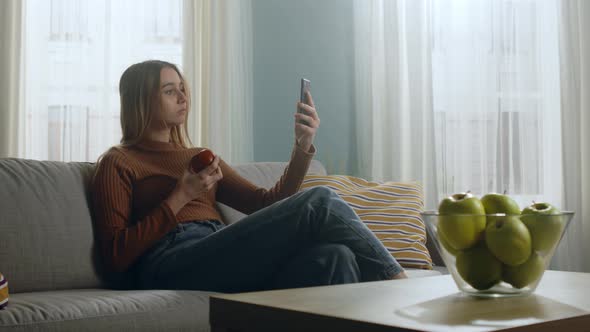 Young Girl with Red Apple Sits on Couch and Takes Selfie on Cell Phone