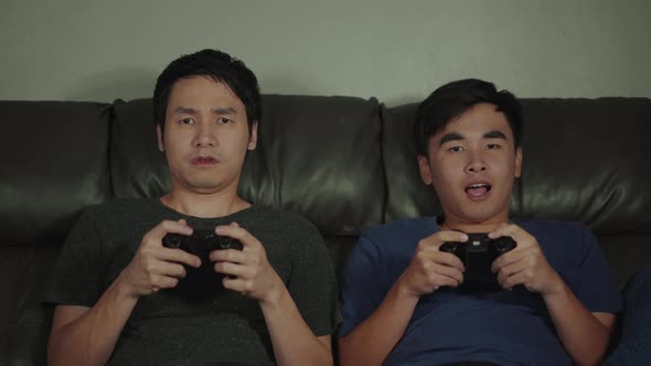 two man playing video games while sitting on sofa. win and lose emotions