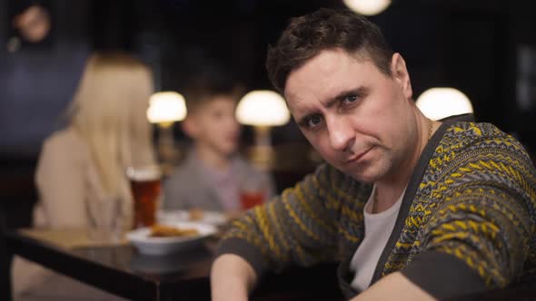 Sad Caucasian Man Sighing Looking at Camera Sitting in Restaurant with Woman and Boy alt