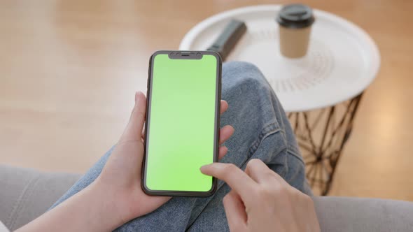 Woman holding mockup smartphone green screen with type message on the sofa at home. alt