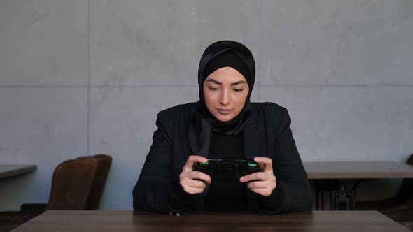 Young Muslim Woman in Hijab Playing Mobile Game in Cyberspace at Cafe