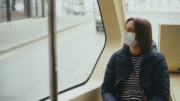 A Young Woman Wearing a Facial Mask Looking at the Window While Riding a Bus
