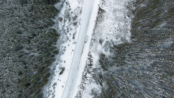 Drone camera rises above road in the mountains and lonely car driving in the snow in Alberta, Canada alt