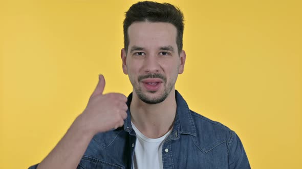 Portrait of Ambitious Young Man Doing Thumbs Up, Yellow Background alt