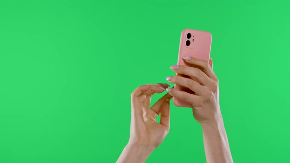 Female Hands Hold the Smartphone Vertically Against the Background of the Green Screen of the Chroma alt