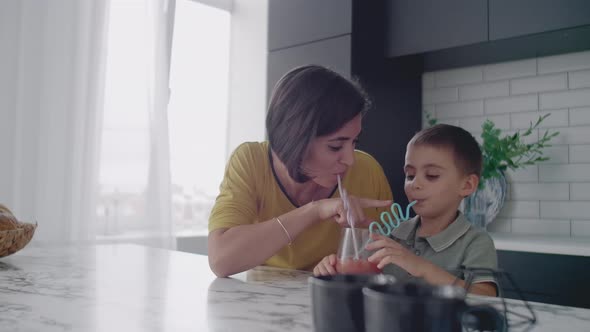 Loving Beautiful Mother and Son Together Smiling Drinking Orange Juice From a Glass Glass Through a alt