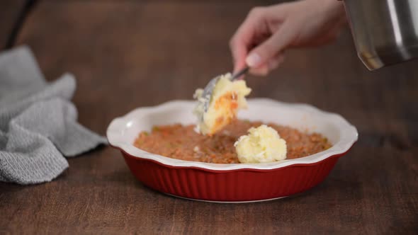 Woman making shepherd's pie. Mashed potatoes being placed on top of minced meat.